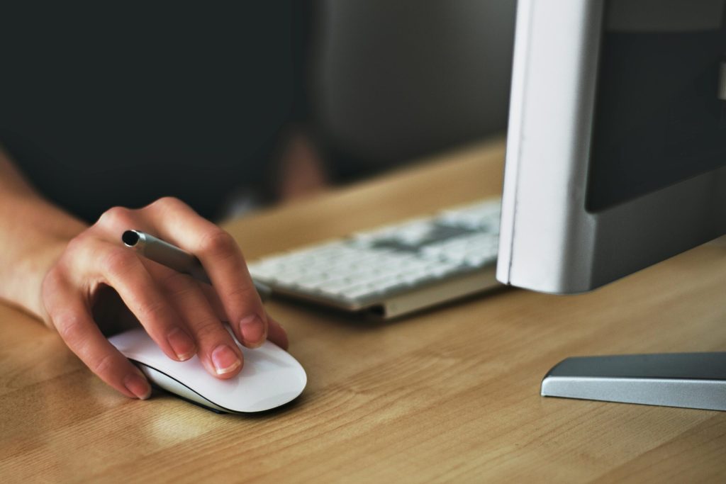Free A hand using a wireless mouse at a modern desk setup with a computer and keyboard. Stock Photo